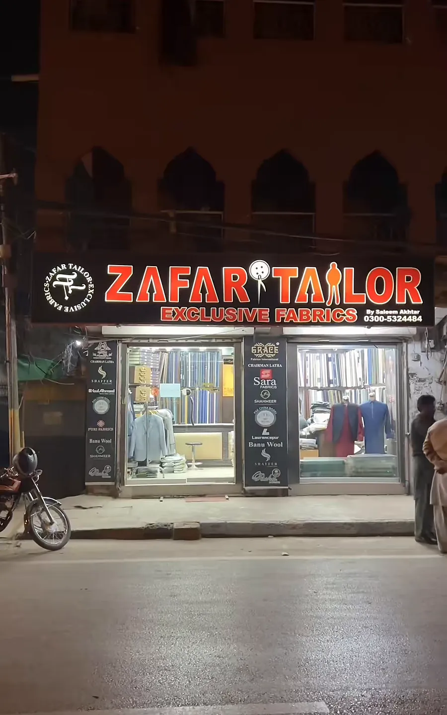 The Zafar Tailor Exclusive Fabrics shopfront at night, its sign lit